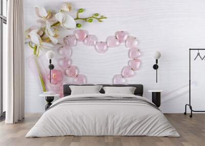 Big rose quartz heart compilated from same pendants, an artificial textile sprig of orchid, two candles lit and silk ribbons create the flat lay composition. Top view, copy space. Wall mural