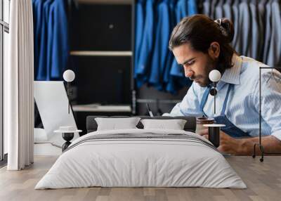 Focused brazilian business man with cup of coffee working in laptop and taking notes inside business store. business, workplace, successful, entrepreneur, occupation concept.. Wall mural