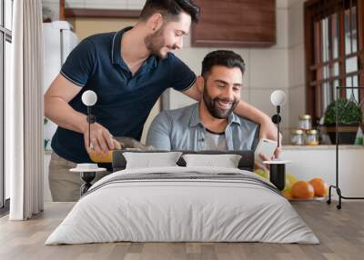 happy gay man serving juice and looking at mobile at table Wall mural