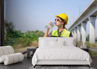 railway engineer or construction worker in hardhat and safety vest,holding paperwork is thirsty in the harsh sunlight,attractive caucasian female wears sunglasses drinking water while working outside Wall mural