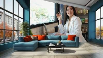 young attractive business woman waving to greeting someone while working with laptop in the coffee shop, concept business, outside work, freelance Wall mural