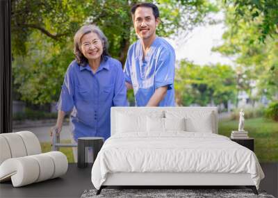 young man caregiver in uniform is taking care of a senior woman while practice walking in the garden Wall mural