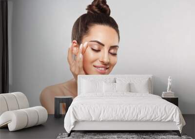 Beautiful smiling woman with healthy smooth facial clean skin applying cosmetic cream and touch own face. Model with  Beauty face. Skin care Moisturizer Facial treatment. Cosmetology. Spa. Wall mural