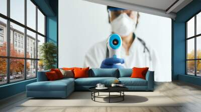 Doctor wearing protective  mask ready to use infrared forehead thermometer  to check body temperature for virus symptoms - epidemic virus outbreak concept. Coronavirus.Thermometer gun Wall mural