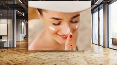 Suntan lotion woman applying sunscreen solar cream. Beautiful happy cute woman  applying suntan cream to her nose. Wall mural