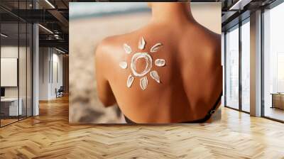 Woman Applying Sun Cream on Tanned  Shoulder In Form Of The Sun. Sun Protection.Sun Cream. Skin and Body Care. Girl Using Sunscreen to Skin. Female Holding Suntan Lotion and Moisturizing Sunblock. Wall mural