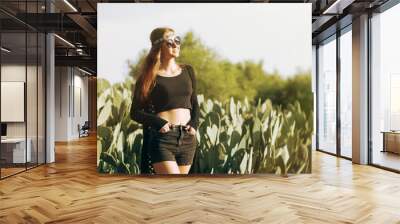 Young female in hippie clothes, sunglasses and headband standing Wall mural