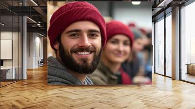 A young man with a beard smiles brightly, standing in a warehouse setting. Wall mural