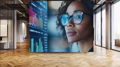 Focused woman in glasses looking at financial charts on screen. Wall mural