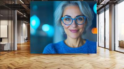 Smiling woman with grey hair wearing blue glasses. Wall mural