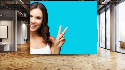 Attractive woman showing two fingers or victory hand sign gesture isolated on aqua blue green studio background. Smiling gesturing brunette girl. Wide banner composition with mock up copy space Wall mural