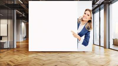 Happy smiling young businesswoman in blue confident suit, showing blank signboard with copyspace empty area for slogan or advertise text, isolated over grey background. Blond model in business concept Wall mural