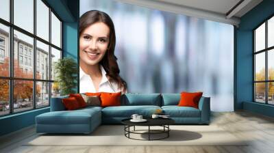 Portrait of happy smiling young cheerful brunette businesswoman, with blank copy space for slogan or some text, over blured office background. Success in business concept. Wall mural