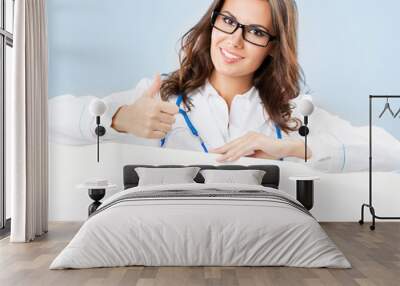 Portrait of happy smiling young female doctor eye wear glasses, spectacles showing blank signboard, isolated over blue background. Wall mural