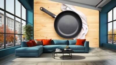 Frying pan and kitchen towel on a wooden background. Top view. Wall mural