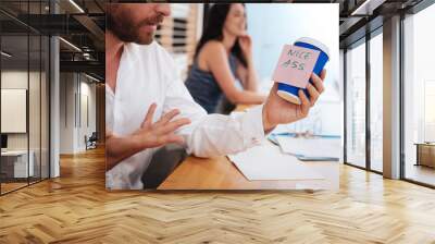 Bafflement. Surprised beaded man holding a cup with a sticker and his secretary sitting in the background Wall mural