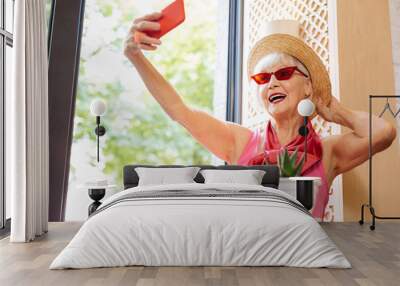 Beautiful accessory. Cheerful positive woman touching her hat while taking a selfie Wall mural