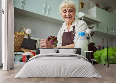 Cheerful old woman in apron cooking dinner at home Wall mural