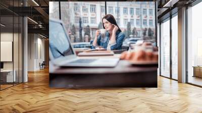 Dreaming about you. Relaxed young woman sitting in cafe and touching her neck while holding cup near mouth Wall mural