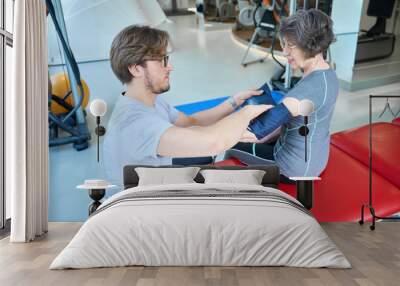 Employee of fitness clinic measures blood pressure of elderly woman Wall mural