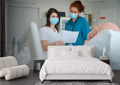 Female doctors with sheet of paper near sick man in intensive care ward Wall mural