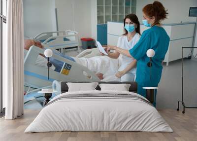 Female doctors with sheet of paper talking to male patient in chamber Wall mural