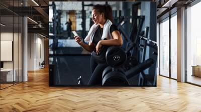 Joyful young woman using smartphone during workout indoors Wall mural