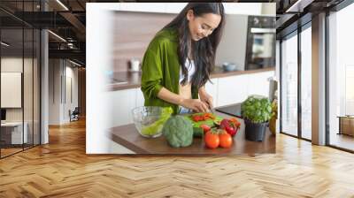 Smiling young woman slicing carrots and tomatoes Wall mural