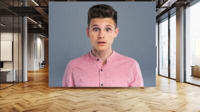 Unexpected information. Close up of a pleasant teenage boy staring wide-eyed having heard some unexpected news while posing isolated on a blue-grey background Wall mural