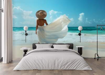 A woman wearing a flowing white beach cover-up and wide-brimmed sun hat, standing on a sandy beach with the ocean waves gently crashing in the background, under a clear blue sky Wall mural