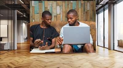 two african young men sitting down using laptop to work online Wall mural