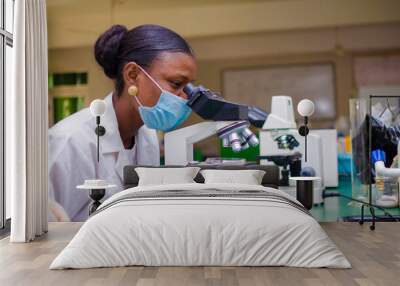 young african scientist looking through a microscope in the laboratory about the vaccine she is working on. Wall mural