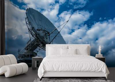 A satellite dish is pointed towards the sky. The sky is cloudy and the sun is not visible Wall mural