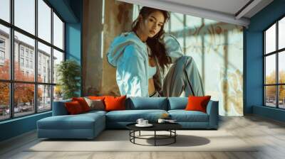 Lonely young woman sitting on the floor in an empty abandoned building wearing a hoodie and pants Wall mural