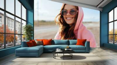 Smiling woman in pink hoodie and sunglasses standing in desert landscape on sunny day Wall mural