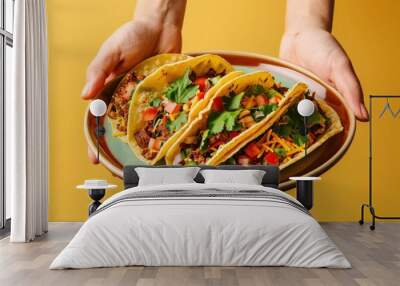 Three colorful tacos topped with fresh vegetables held on a plate against a vibrant yellow background Wall mural