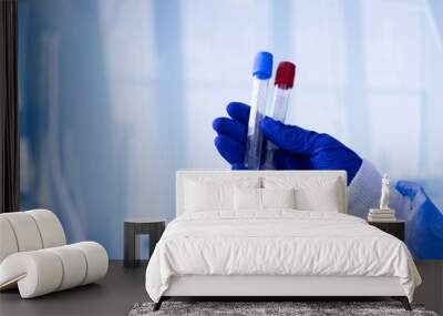 A person is holding two tubes of blood in a blue glove Wall mural