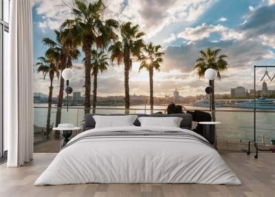 Beautiful shot of a caucasian woman sitting enjoying the sunset in front of a promenade in Malaga. Wall mural