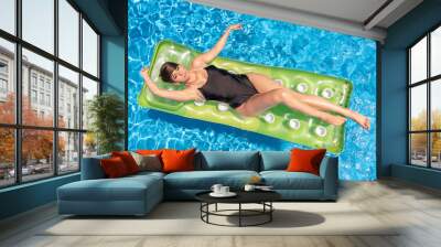 Beautiful young woman in a bikini with short hair lying on a green water mat in a pool enjoying the sun Wall mural