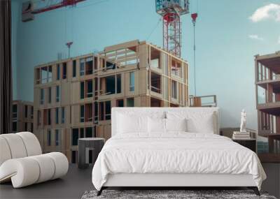 A construction site with wooden-framed buildings under development, featuring a prominent crane lifting materials against a clear blue sky. Wall mural