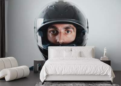 A person gazes directly at the camera, wearing a sleek black motorcycle helmet against a plain background, exuding safety and focus. Wall mural