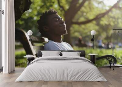 A relaxed individual savors a sunny day on a park bench, eyes closed and soaking in the warm rays, with greenery creating a serene backdrop. Wall mural