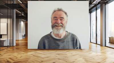 A smiling elderly man with a grey sweater and white beard stands against a clean, light background, exuding warmth and happiness. Wall mural