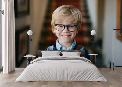 A smiling young boy with glasses holding a stack of books, standing in a warmly lit hallway, showcasing his readiness and excitement for learning. Wall mural