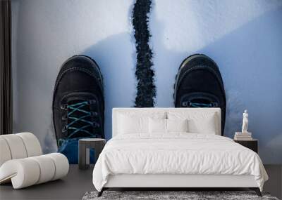 A stylish pair of black boots featuring blue laces is standing in the snow Wall mural