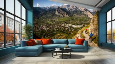 RIDDES, SWITZERLAND. Two men ride mountain bikes along a narrow exposed trail in the Swiss Alps. The dramatic cliff in the background is the Haut de Cry. Wall mural