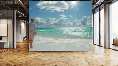 Man on sunny beach enjoying picturesque ocean view with turquoise waters and blue sky. Wall mural