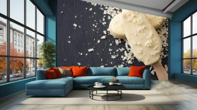 Summer desserts and cold snacks concept with two ice cream bars on a stick or lollies, surrounded by white chocolate shavings  on a dark black stone background with copy space Wall mural