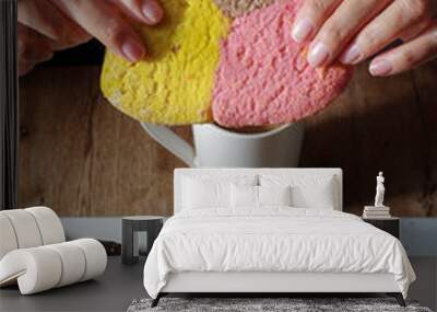 Woman's hand taking a piece of Mexican sweet bread from a white plate on a wooden table. Concept of hands handling food, eating a three color cookie front view vertical. Wall mural