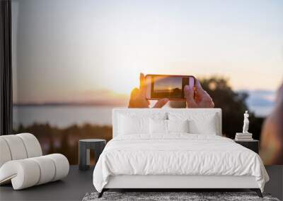 Woman taking a photo with her mobile phone at sunset Wall mural